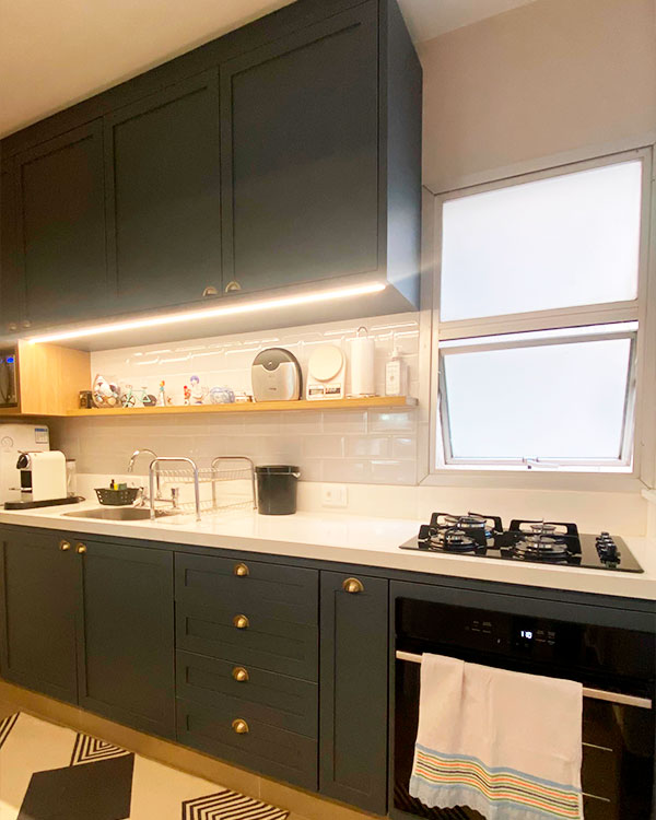 Cozinha planejada branca com bancada em pedra e armários superiores, instalada em casa de veraneio no Centro de Itapema SC